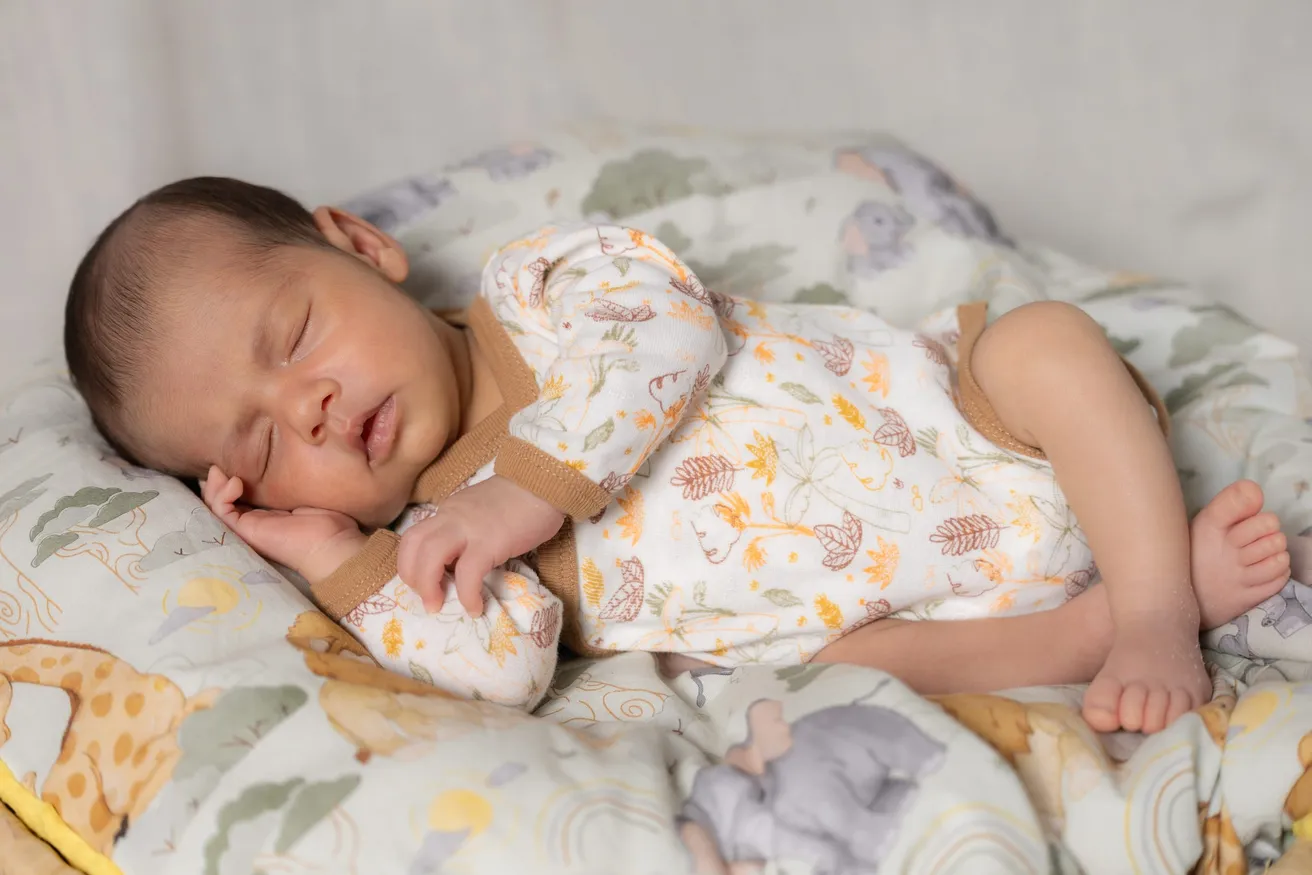 Le nouveau-né dort sur le côté, en pyjama fleuri, sur un coussin à motifs d’animaux