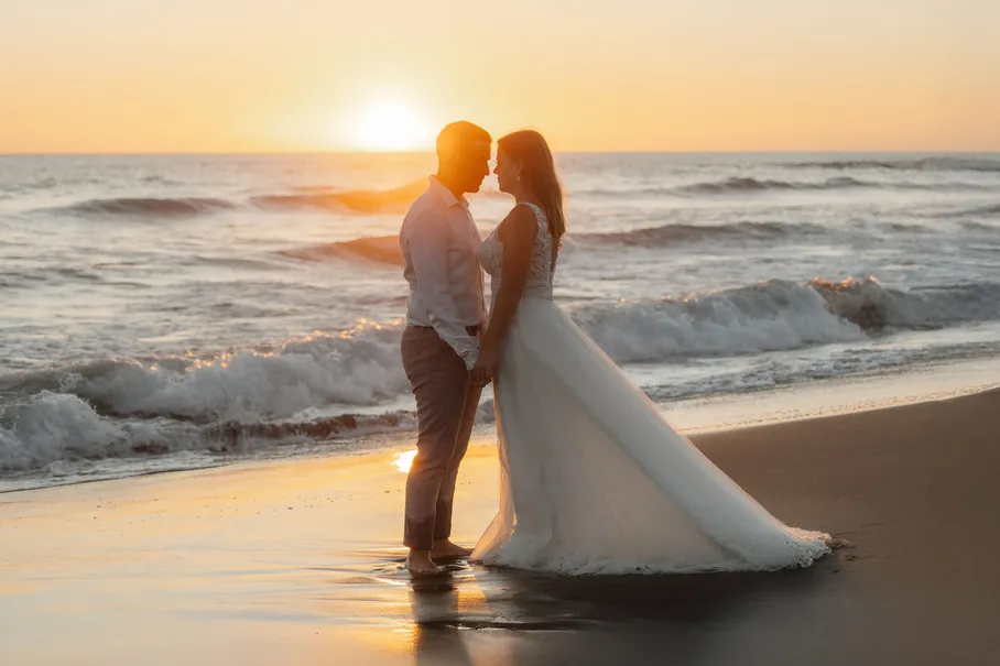 Les mariés s’embrassent à contre-jour, le soleil se couche sur la mer