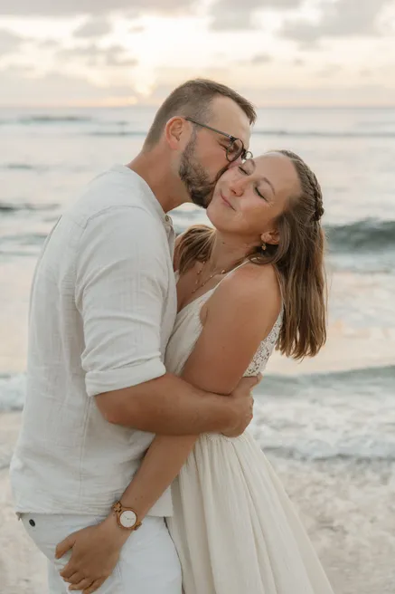 Un couple enlacé sur la plage, il l’embrasse sur la tempe, elle ferme les yeux en souriant