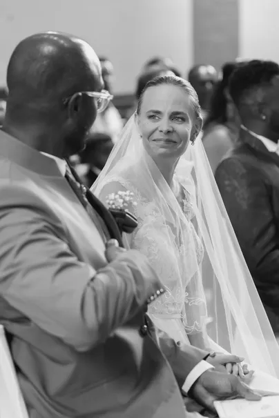 En noir et blanc, la mariée voilée regarde le marié, assis côte à côte à la cérémonie