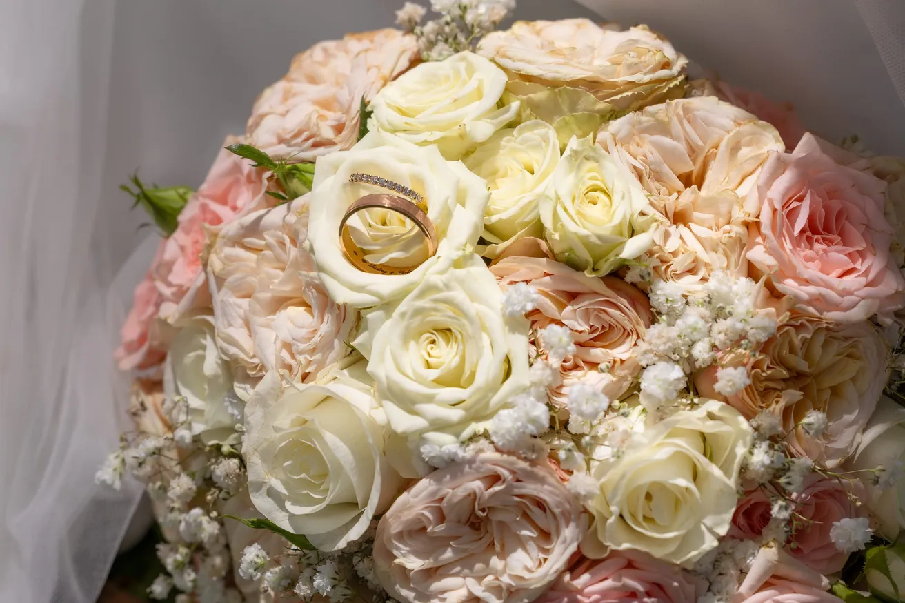 Deux alliances posées au cœur d’un bouquet de roses blanches et rose poudré