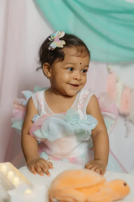 Une petite fille en robe pastel, une barrette fleur dans les cheveux, sourit en regardant de côté