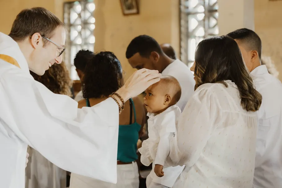 Le prêtre pose la main sur le front de l’enfant, entouré de la famille vêtue de blanc