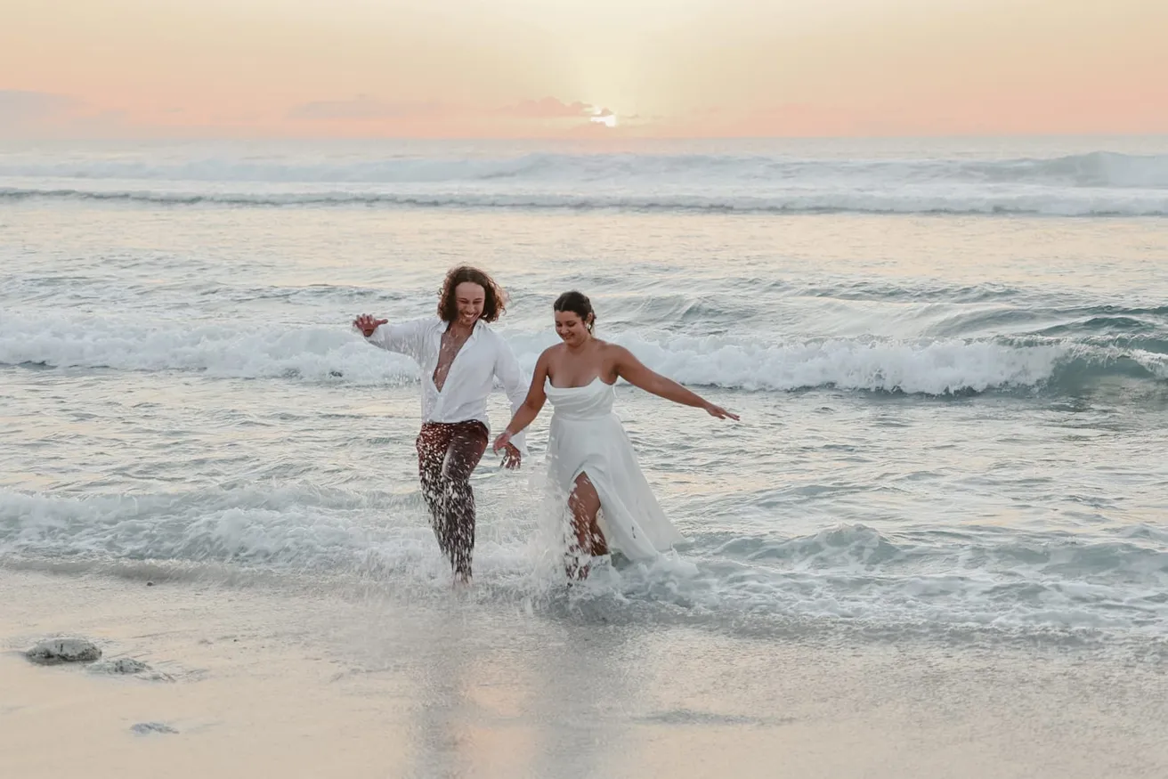 Les mariés courent dans l’écume au coucher du soleil, la mariée soulève sa robe