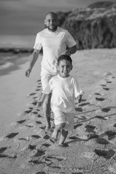 En noir et blanc, un père et son fils courent côte à côte sur la plage