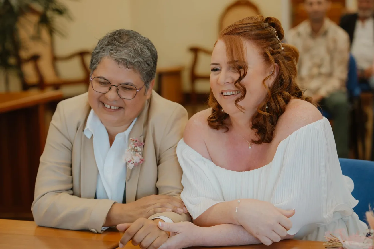 Les mariées assises côte à côte à une table de mairie, souriantes et complices