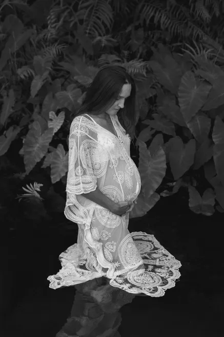 En noir et blanc, future maman en tunique de dentelle au milieu de grandes feuilles sombres