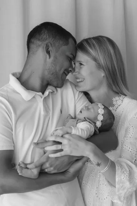En noir et blanc, un couple front contre front tient son nouveau-né entre eux