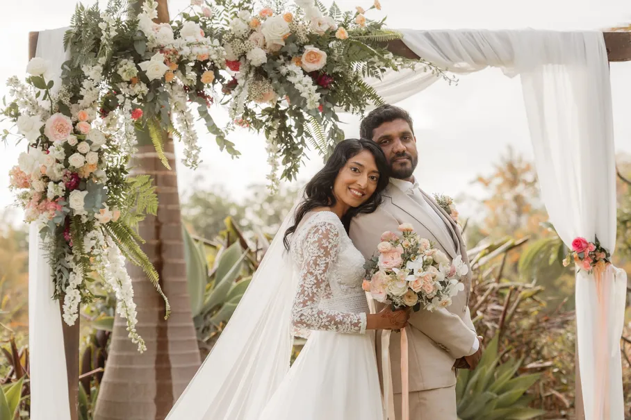 La mariée pose la tête contre l’épaule du marié sous l’arche fleurie