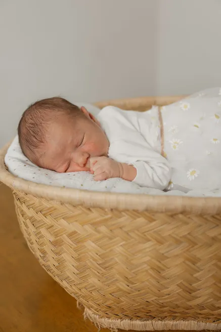 Nouveau-né endormi dans un couffin en osier, pyjama à petites fleurs