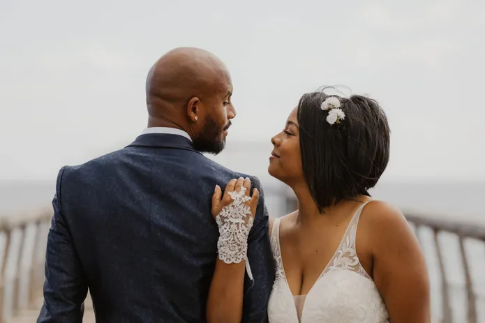Le marié de dos, la mariée pose sa main gantée de dentelle sur son épaule et le regarde