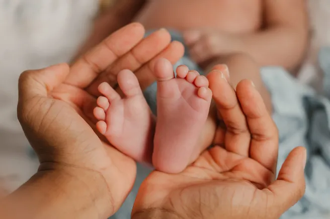 Deux mains d’adulte en coupe tiennent délicatement les petits pieds du nouveau-né