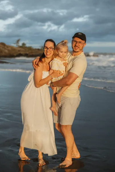 Un couple porte sa petite fille entre eux, pieds nus sur le sable noir mouillé