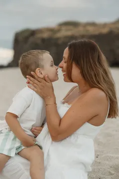Une mère tient le visage de son petit garçon et l’embrasse, nez contre nez sur la plage