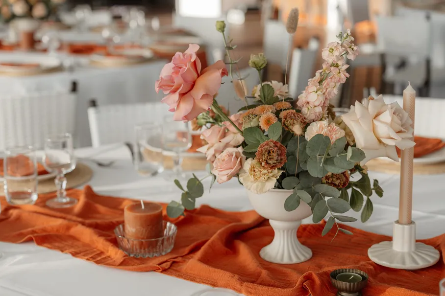 Centre de table de roses et d’eucalyptus dans une coupe blanche, sur un chemin de gaze orange