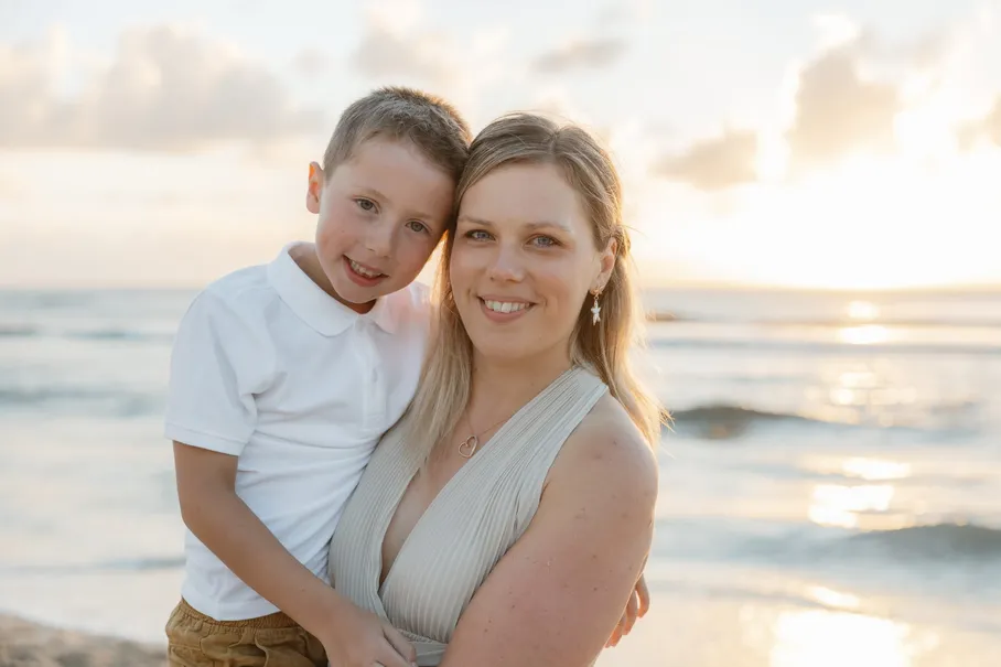 Une mère et son fils posent joue contre joue, devant la mer au soleil couchant