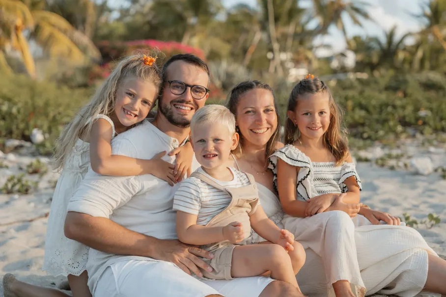 Les parents et leurs trois enfants blottis ensemble sur le sable, devant la végétation