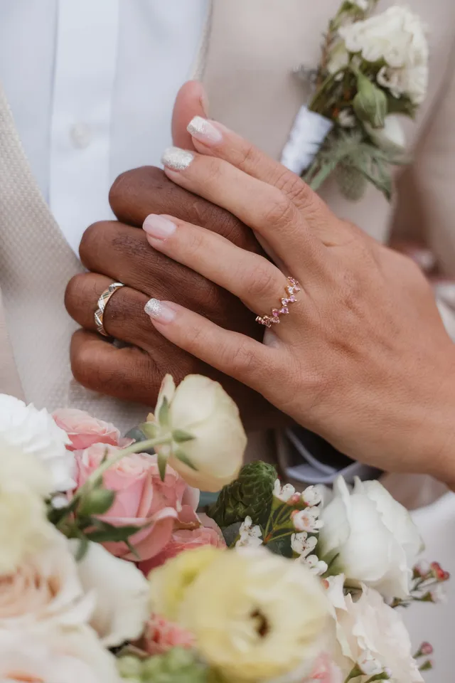 Les mains des mariés l’une sur l’autre, alliances aux doigts, au-dessus du bouquet