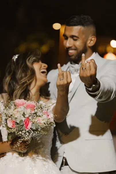 Les mariés rient en montrant leurs alliances, un bouquet de roses pâles au premier plan