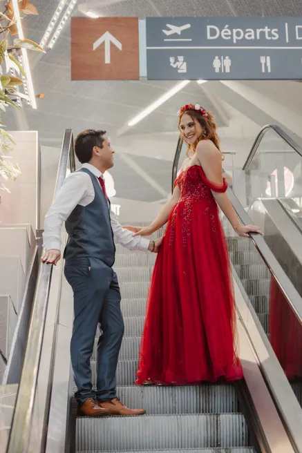 Les mariés sur un escalator sous le panneau des départs, la mariée en robe rouge