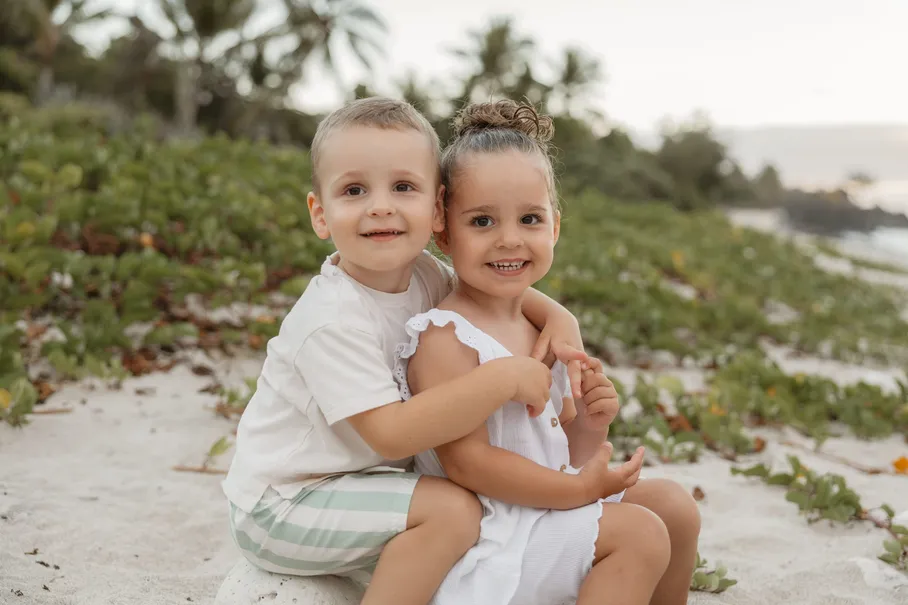 Deux enfants accroupis sur le sable, les palmiers derrière eux