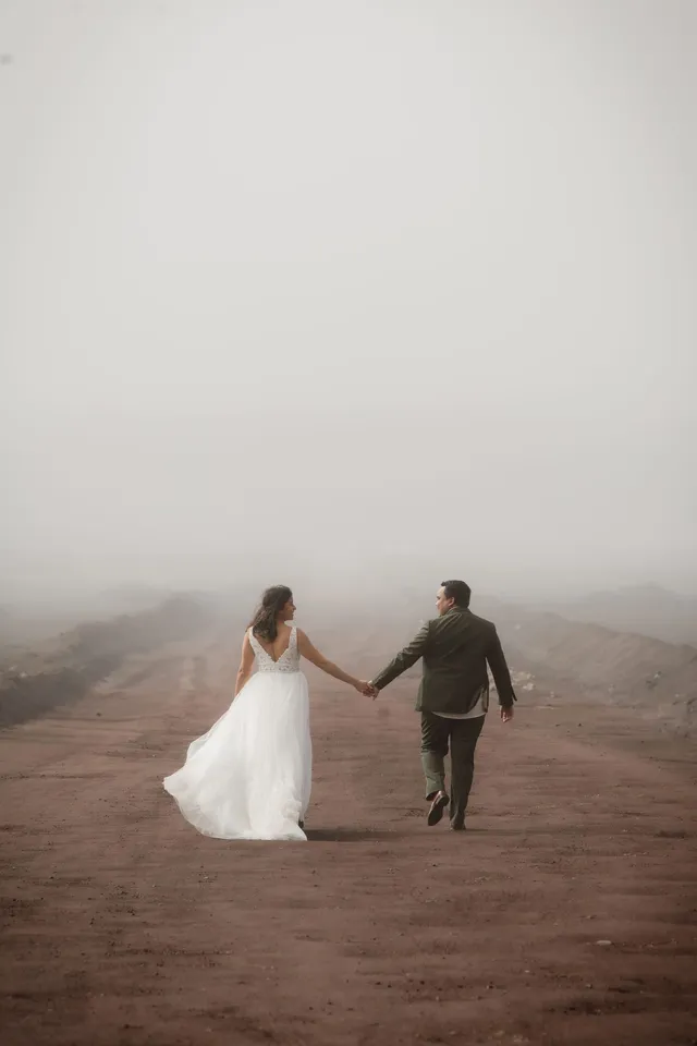 De dos, les mariés s’éloignent main dans la main sur une piste de terre rouge noyée de brume