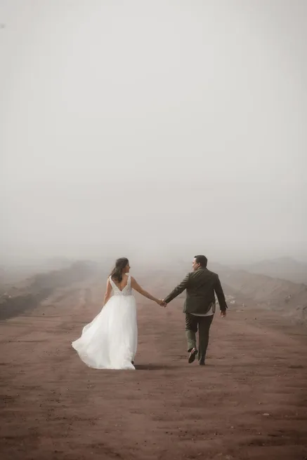 De dos, les mariés s’éloignent main dans la main sur une piste de terre rouge noyée de brume