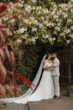 Les mariés enlacés sous un arbre fleuri, longue traîne de voile posée sur le sol
