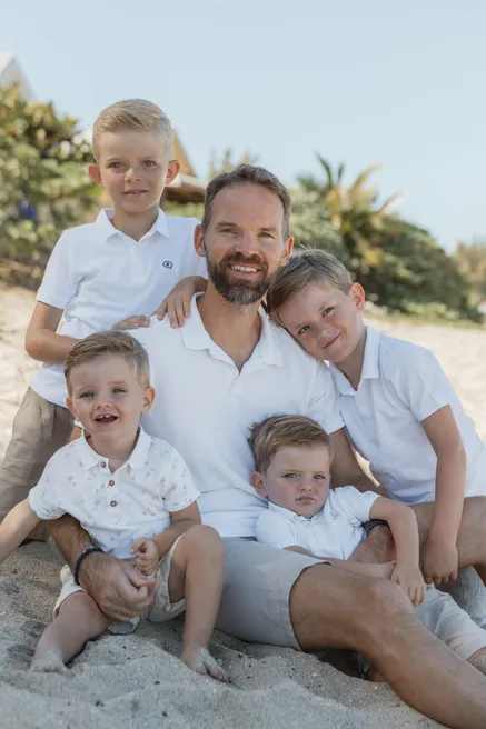 Un père assis sur le sable, entouré de ses quatre petits garçons en chemises blanches