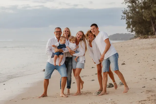 Trois générations marchent ensemble, pieds nus sur le sable, au bord de l’eau