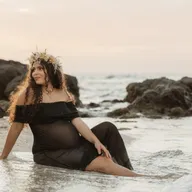 Future maman en robe noire et couronne de fleurs, sur les rochers face à la mer