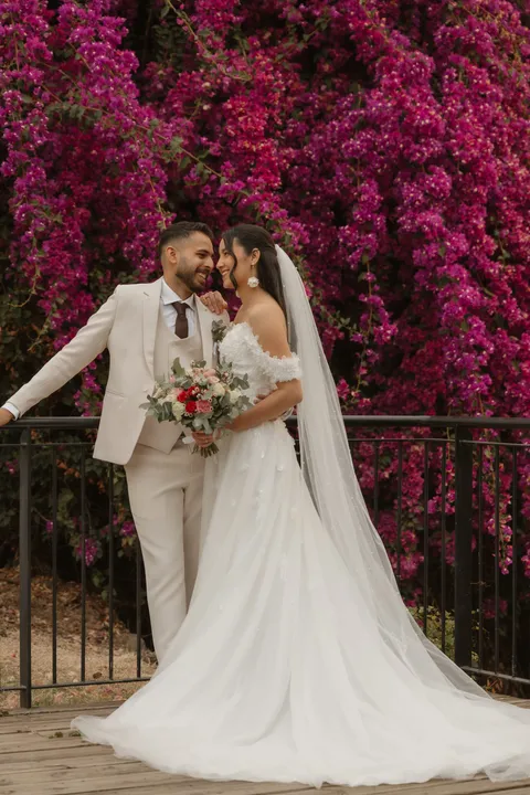La mariée, le bouquet à la main, se tourne vers son mari devant un mur de bougainvilliers en fleurs